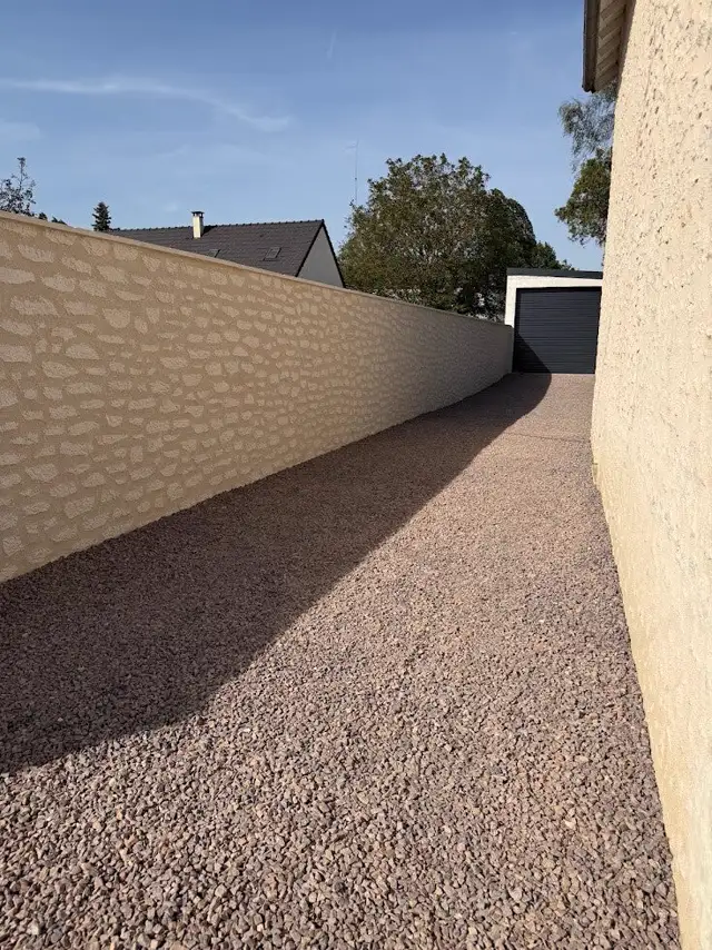 Clôture enduite en décopierre le long d'une allée gravillonnée