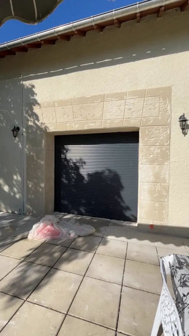 Garage effet pierre avec porte roulante noire et appliques extérieures